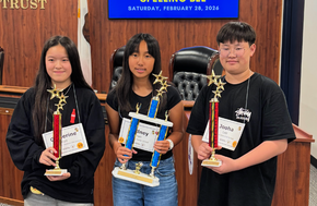 Three students proudly hold trophies after a spelling bee competition.