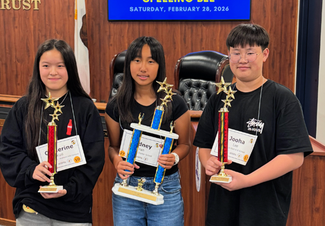 Three students proudly hold trophies after a spelling bee competition.